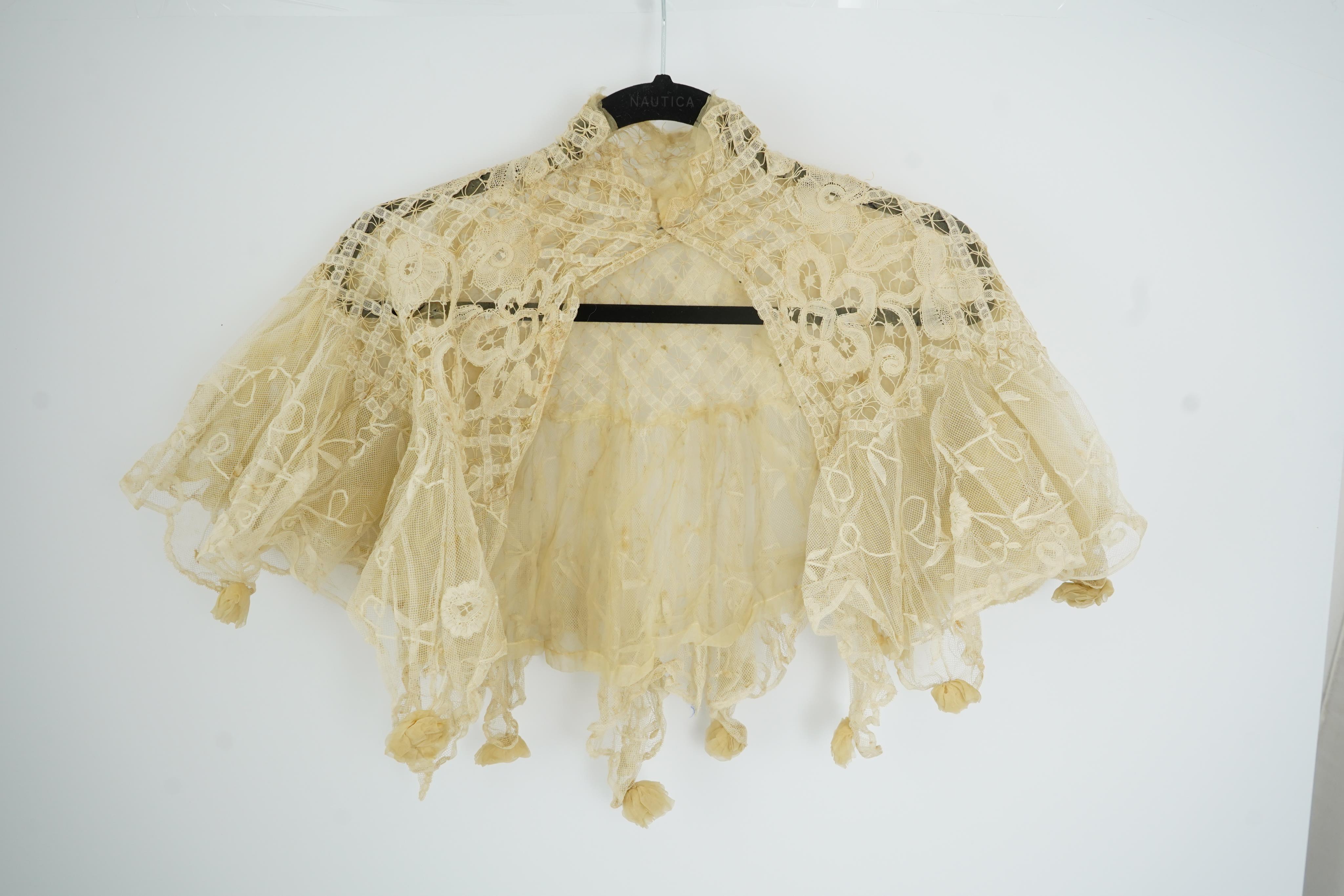 An Edwardian high collared cream tape lace wedding over blouse, made with a deep net frill and cream chiffon rose detail hanging from lower edge, top of collar to rose detail at the front 46cm. Condition - fine silk chif